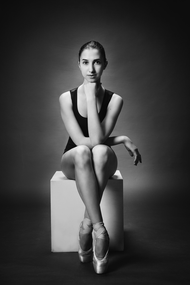 ballerina. A ballerina in a bodysuit and pointe shoes sits on a cube and looking directly von Alexandr