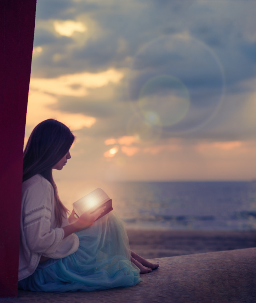 Woman sitting on a beach with illuminated book von Alla Simacheva