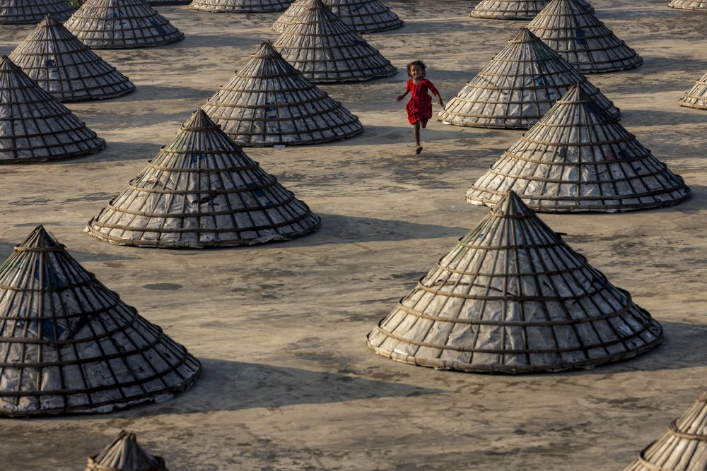 Children run amongst hundreds of traditional rice mills made from bamboo von Azim Khan Ronnie