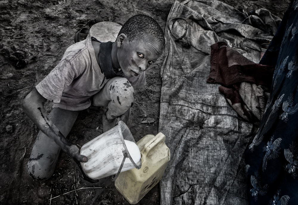 Mundari child passing the freshly milked milk to another container. von Joxe Inazio Kuesta Garmendia